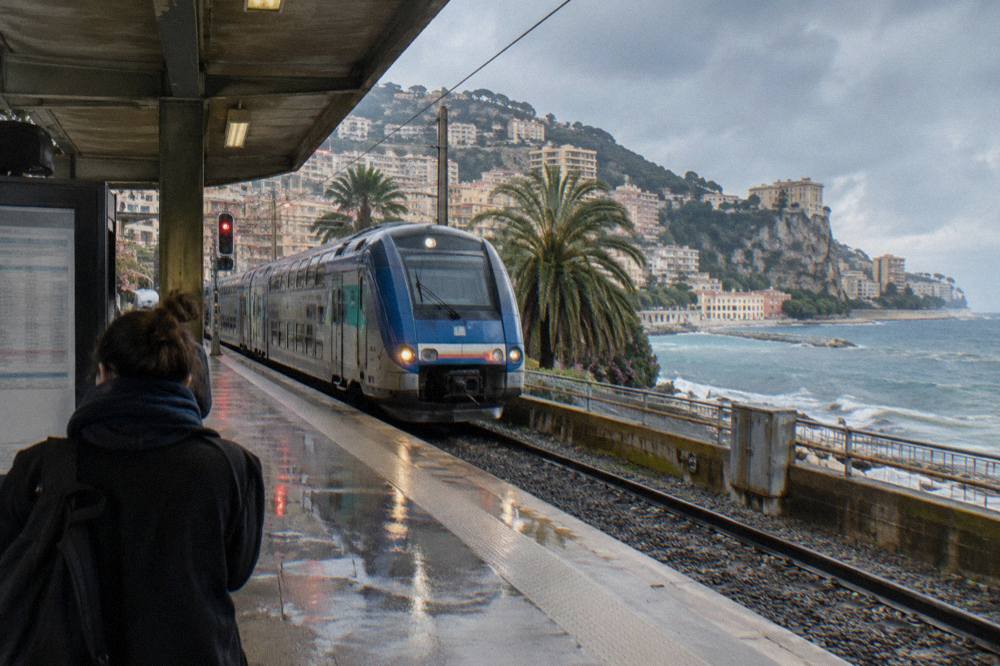 Regional train arriving at a small Riviera station platform above the Mediterranean coast