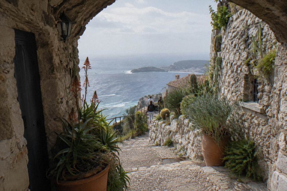Narrow medieval village lane with stone walls and potted plants overlooking the sea