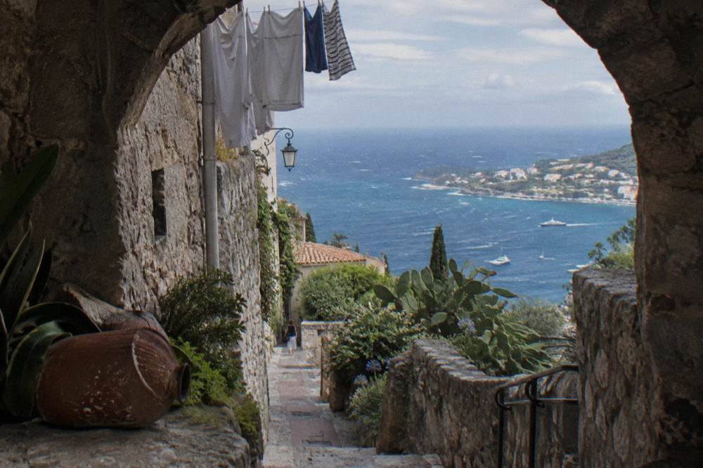 Narrow stone street in a medieval hilltop village with an archway and view toward the Mediterranean