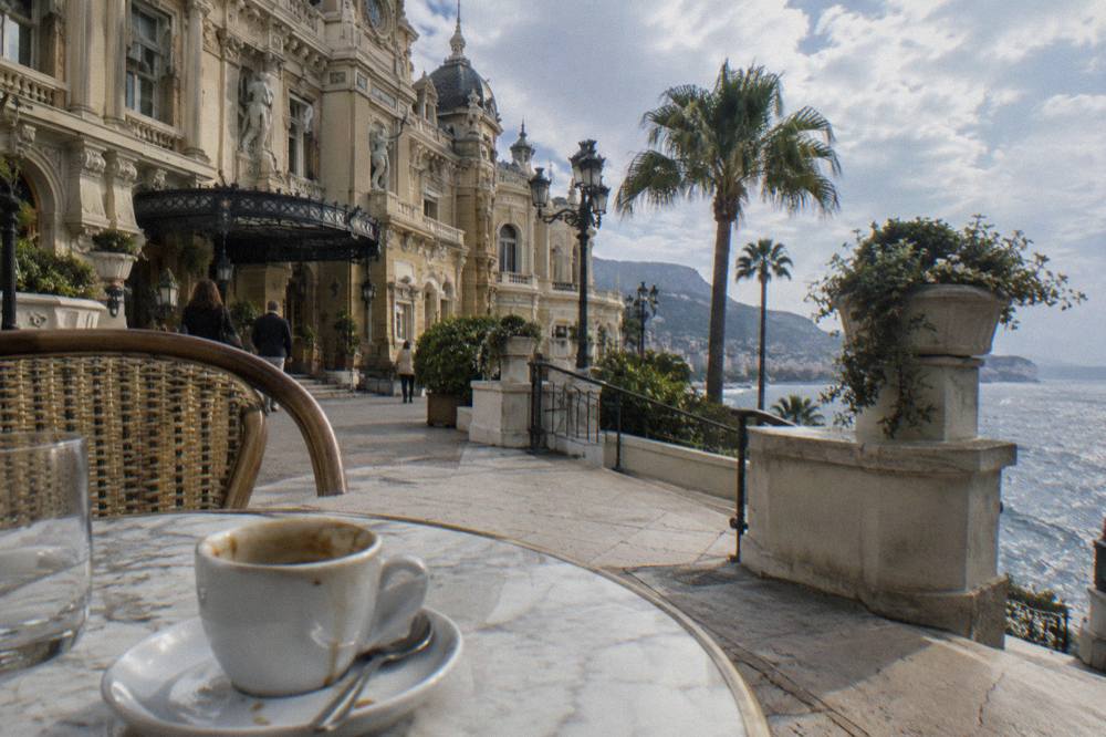 Cafe terrace with small tables and espresso cups beside a stone building facade