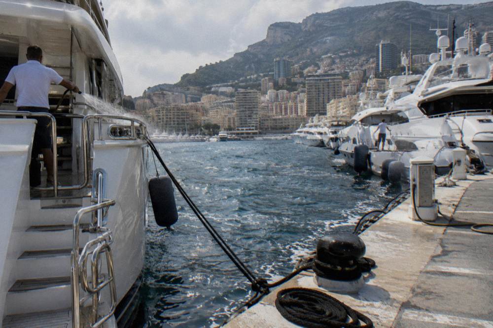 Row of large white motor yachts moored along a harbor quay with hills behind