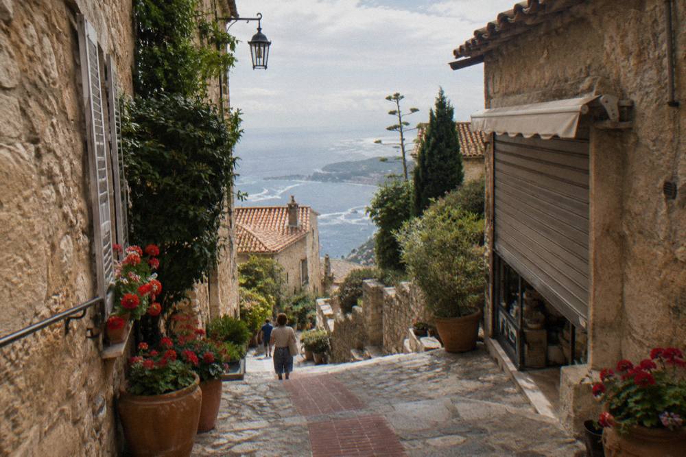 Narrow stone lane in a hilltop village with shops and sea view beyond
