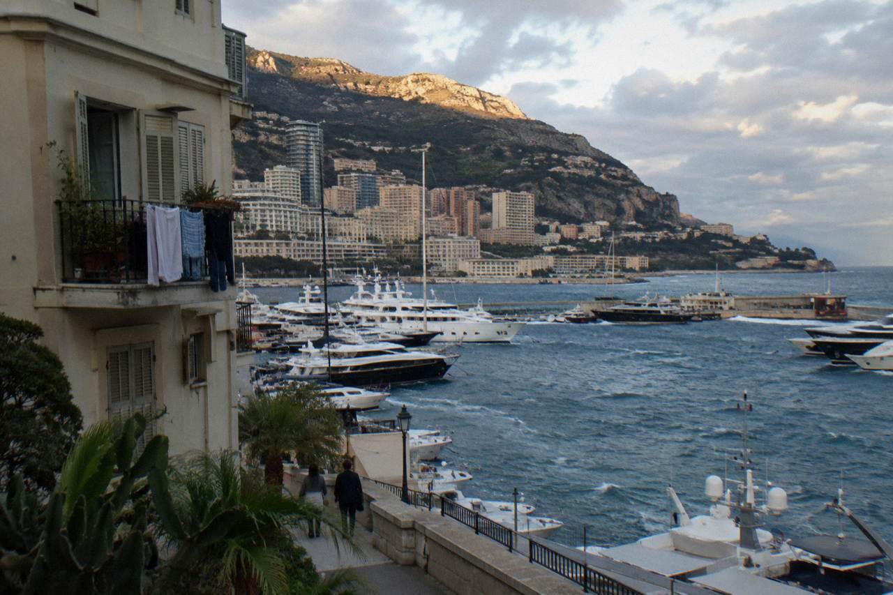 View over Monaco harbor with luxury yachts moored below hillside buildings under a clear sky