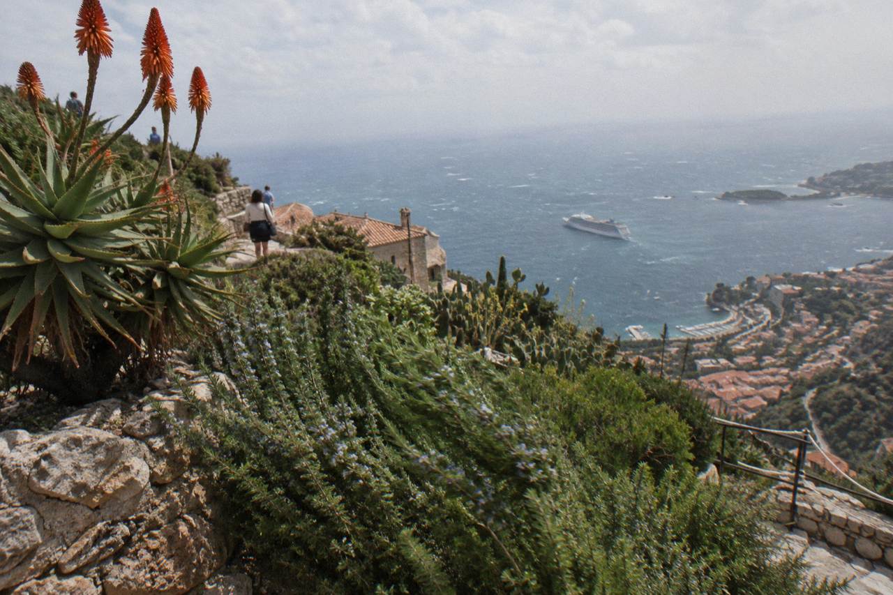 Stone village terraces above the Mediterranean with a cruise ship anchored in the bay below