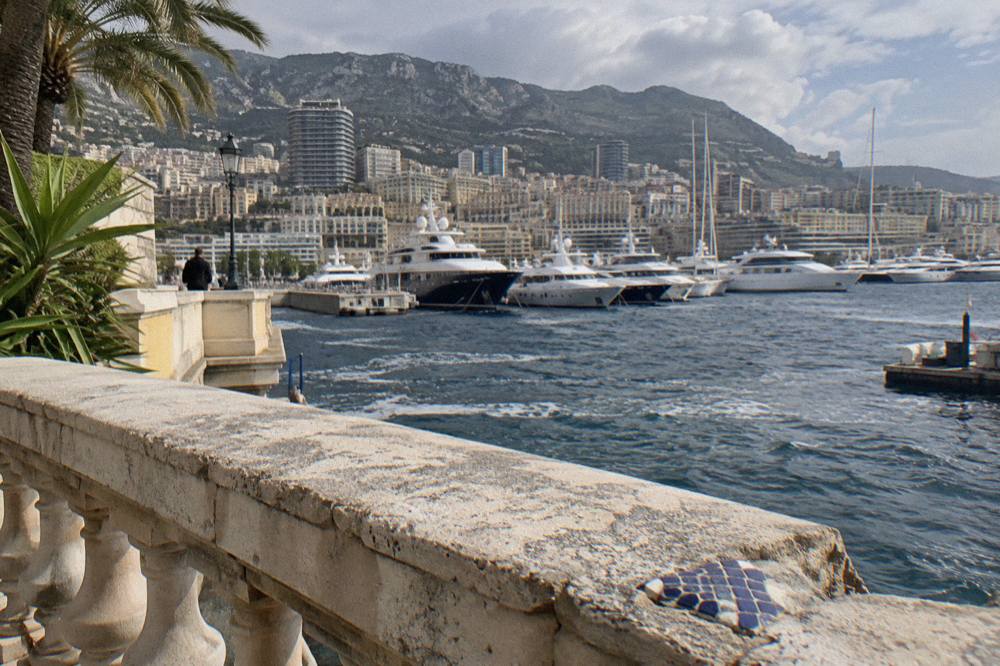 Wide stone terrace overlooking Monaco's harbor with yachts moored along the quays and hills rising behind the town
