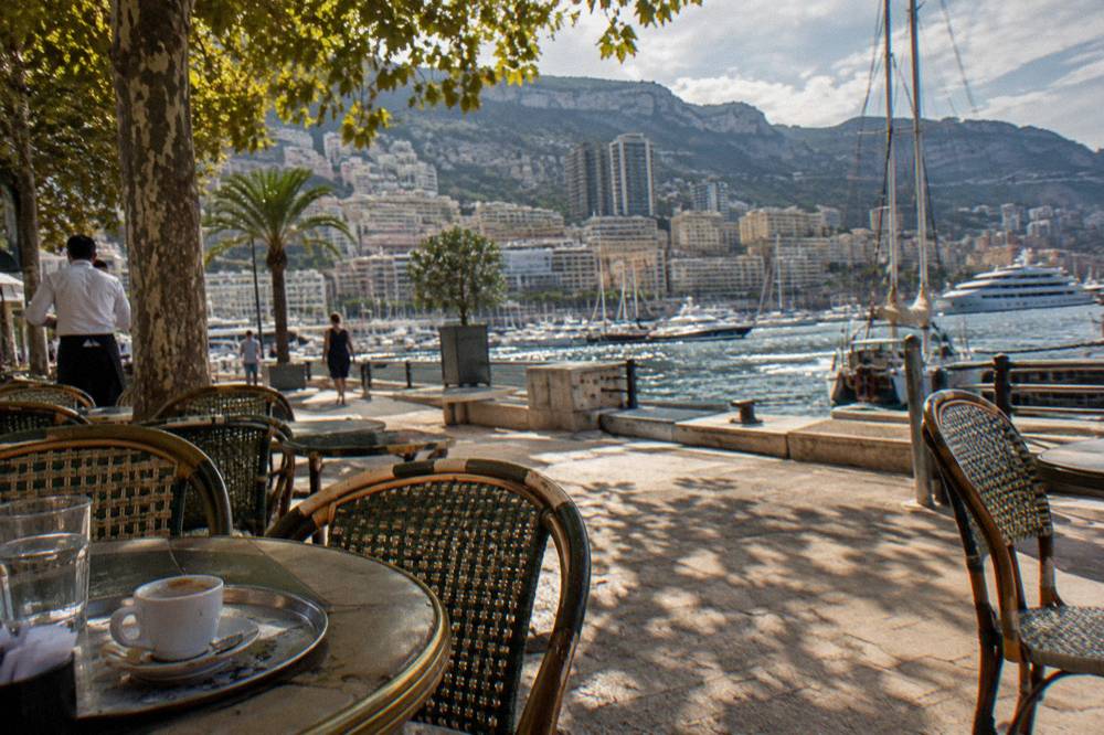Old town square in Nice with ochre facades, cafe tables under plane trees and people strolling in warm light