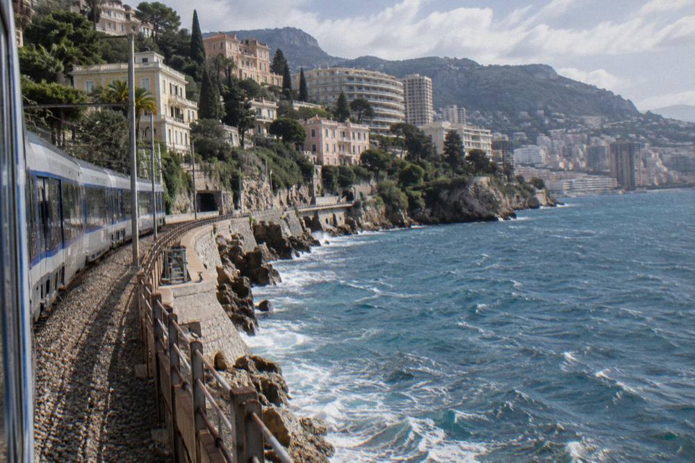 A passenger train platform on the French Riviera with the sea in the background.
