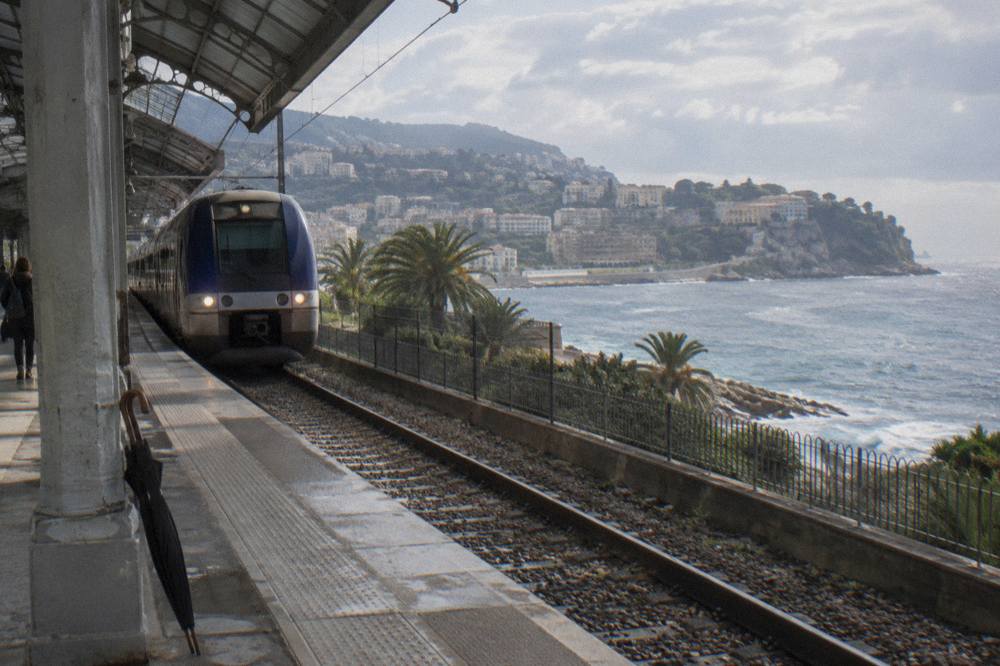 Coastal railway platform overlooking the Mediterranean with a regional train arriving