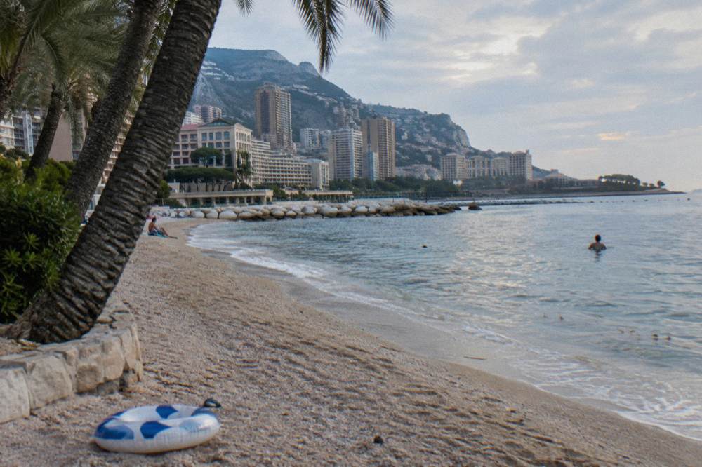 Sandy beach with calm blue water and palm trees along the Larvotto seafront
