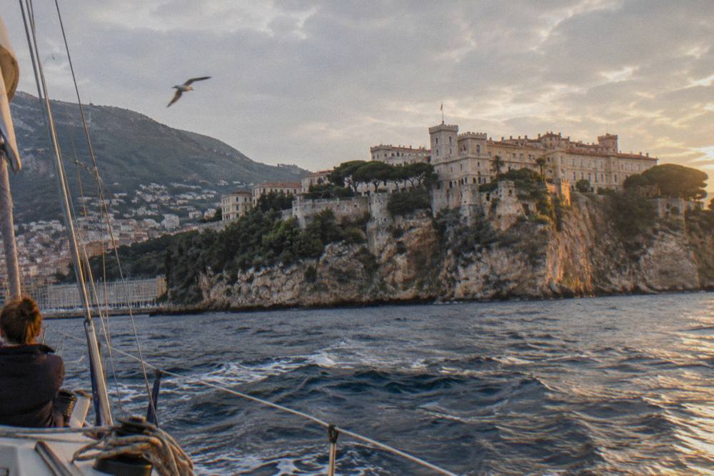 Sailing boat passing below the fortified cliffs of the Rock of Monaco with the old town above