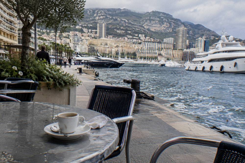 Outdoor cafe tables beside a harbor with yachts moored in the background