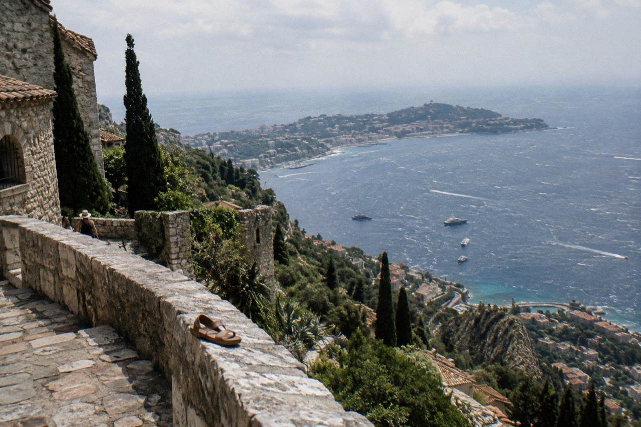 Stone terrace of a hilltop village above the Mediterranean with a walled medieval town in the distance