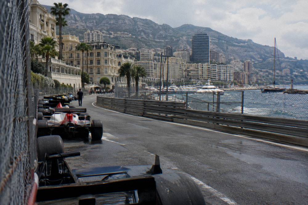 Formula 1 cars parked along the Monaco pit lane with the harbor and hills behind