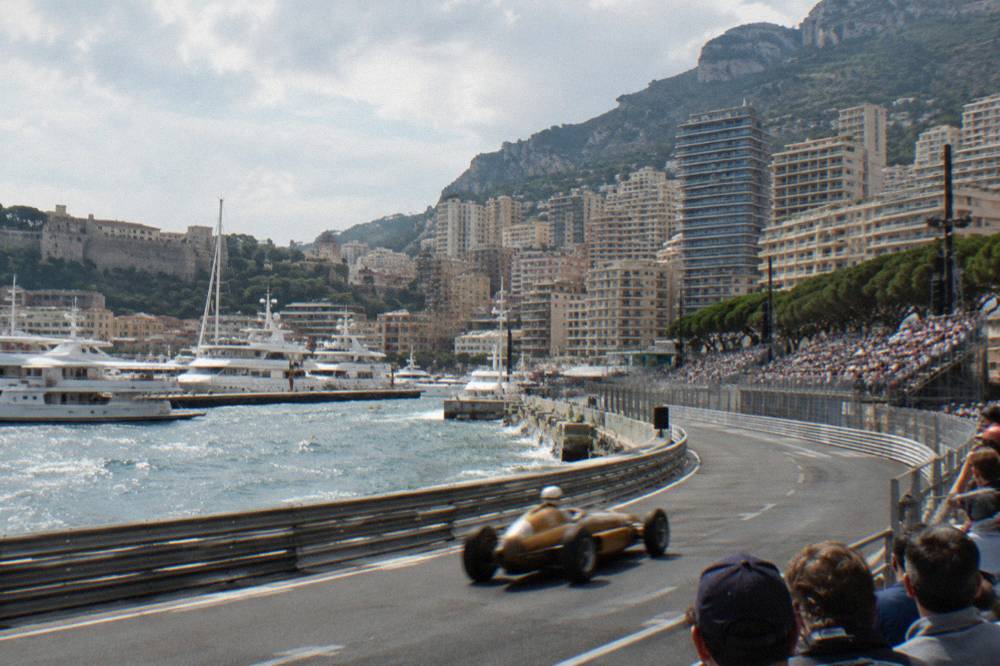 Formula cars racing through the Monaco harbor frontage with spectators in grandstands