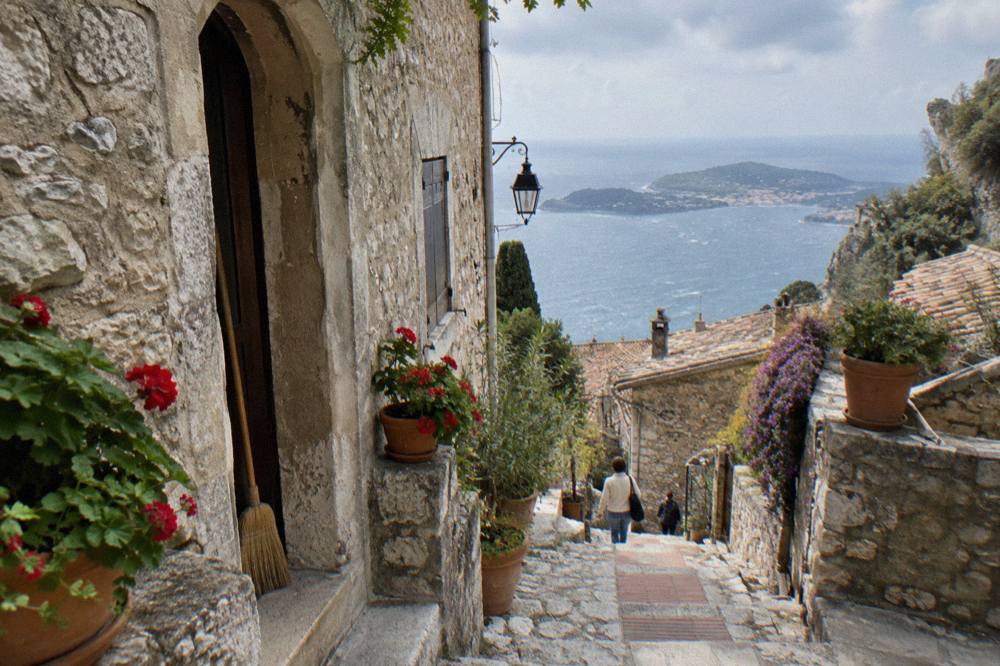 Narrow stone street in Eze village with potted plants and warm light on old walls
