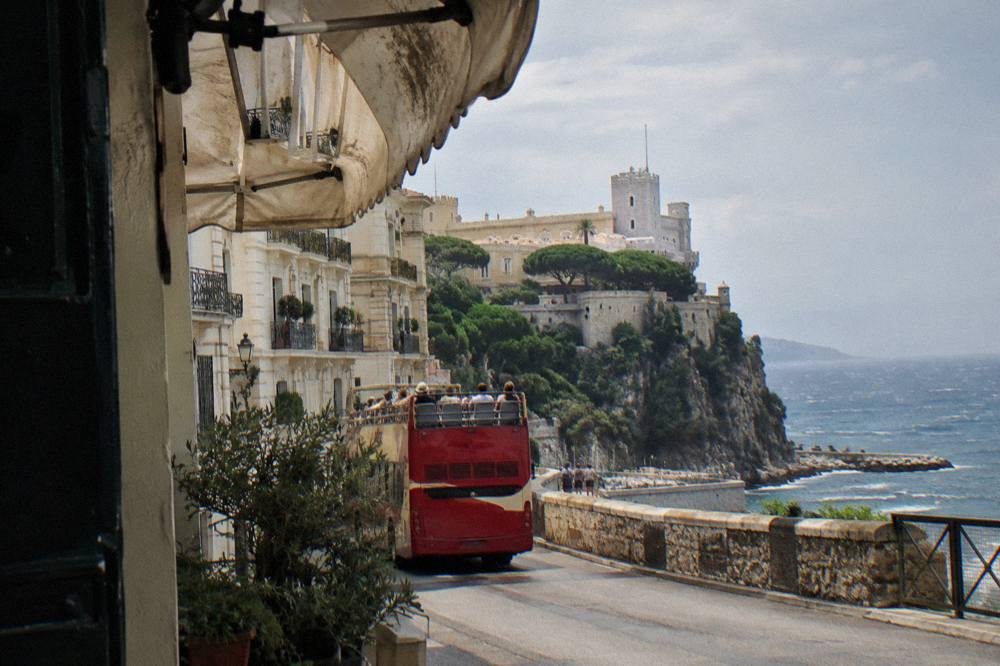 Open-top sightseeing bus driving along a Monaco street with apartment buildings above