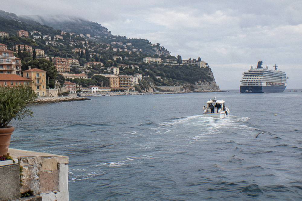Tender boat crossing a calm blue bay toward a cruise ship anchored off a harbour town
