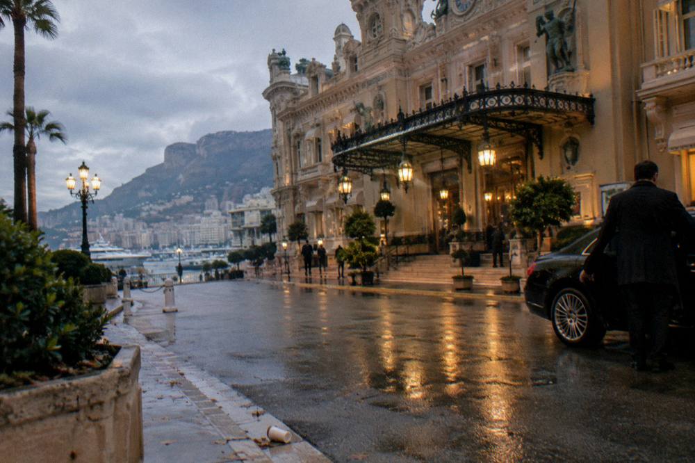 Driver standing beside an open car door in front of Monte Carlo's casino building