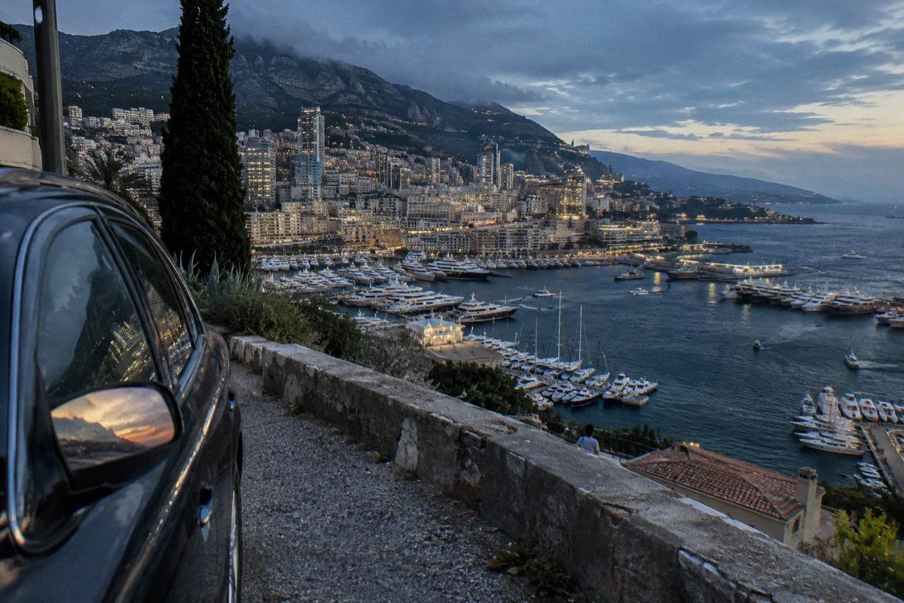 Private car parked on a coastal road above Monaco harbor with luxury yachts below