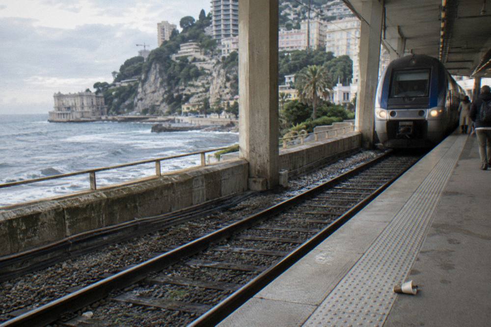 Railway platform beside the sea with a regional train arriving and cliffs in the background