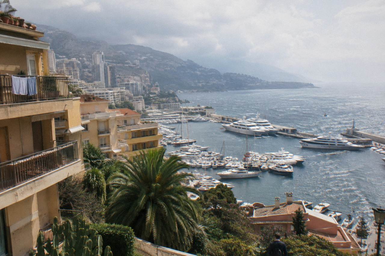 View over Monte Carlo rooftops toward the harbor with yachts moored along the quays
