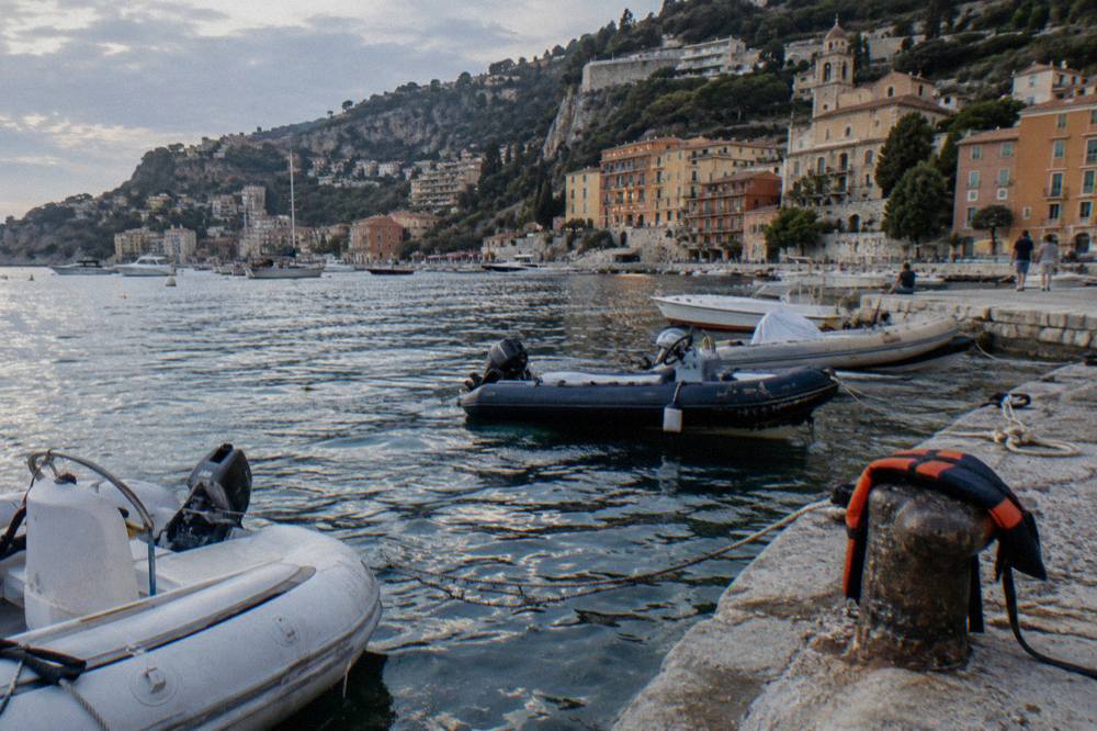Tender boats crossing a calm bay toward a village waterfront with pastel buildings