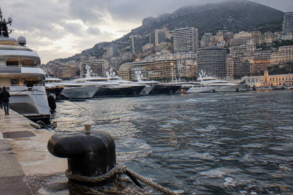 Harbor at dusk with luxury yachts and hillside buildings lit against the evening sky