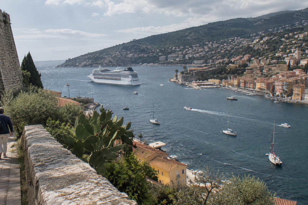 Cruise ship anchored in a Mediterranean bay with hillsides rising above a harbor town
