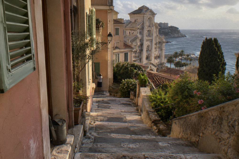 Narrow stepped lane in Monaco-Ville with pastel walls and green shutters at golden hour
