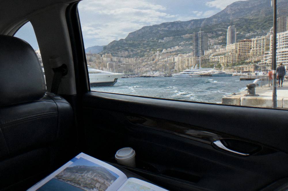 An open tour book resting on the leather back seat of a car facing the sea