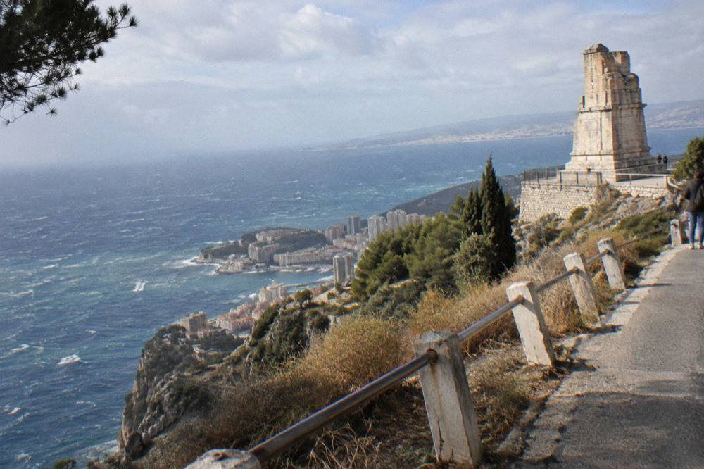A winding cliffside road with guardrail above a deep blue Mediterranean bay