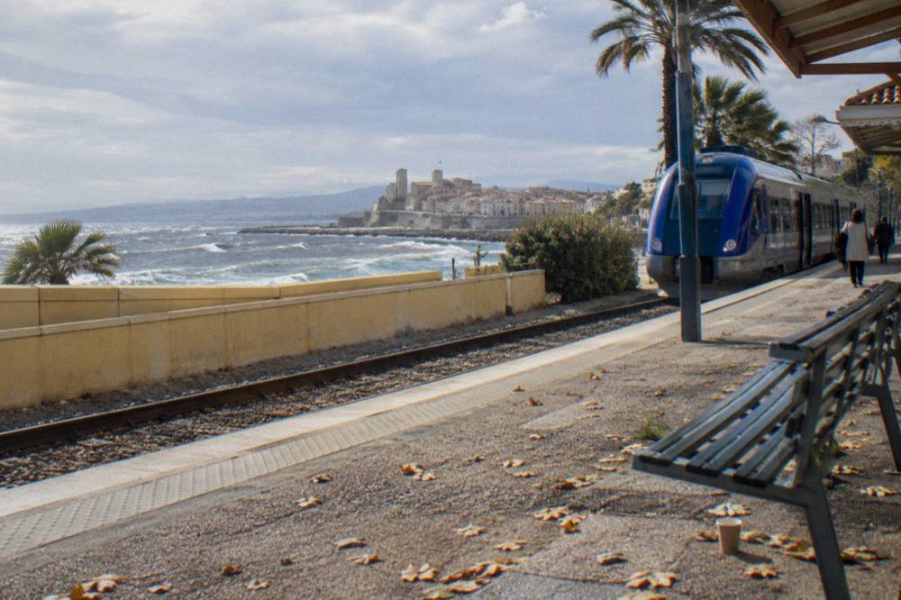 Railway platform beside the Mediterranean with a regional train at a small coastal station