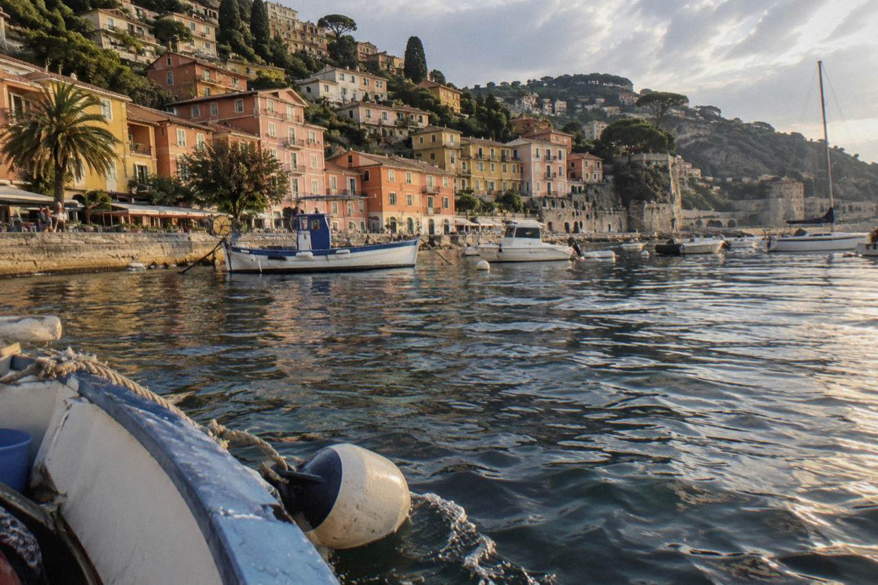 Pastel houses rising above a calm Mediterranean bay with fishing boats at anchor