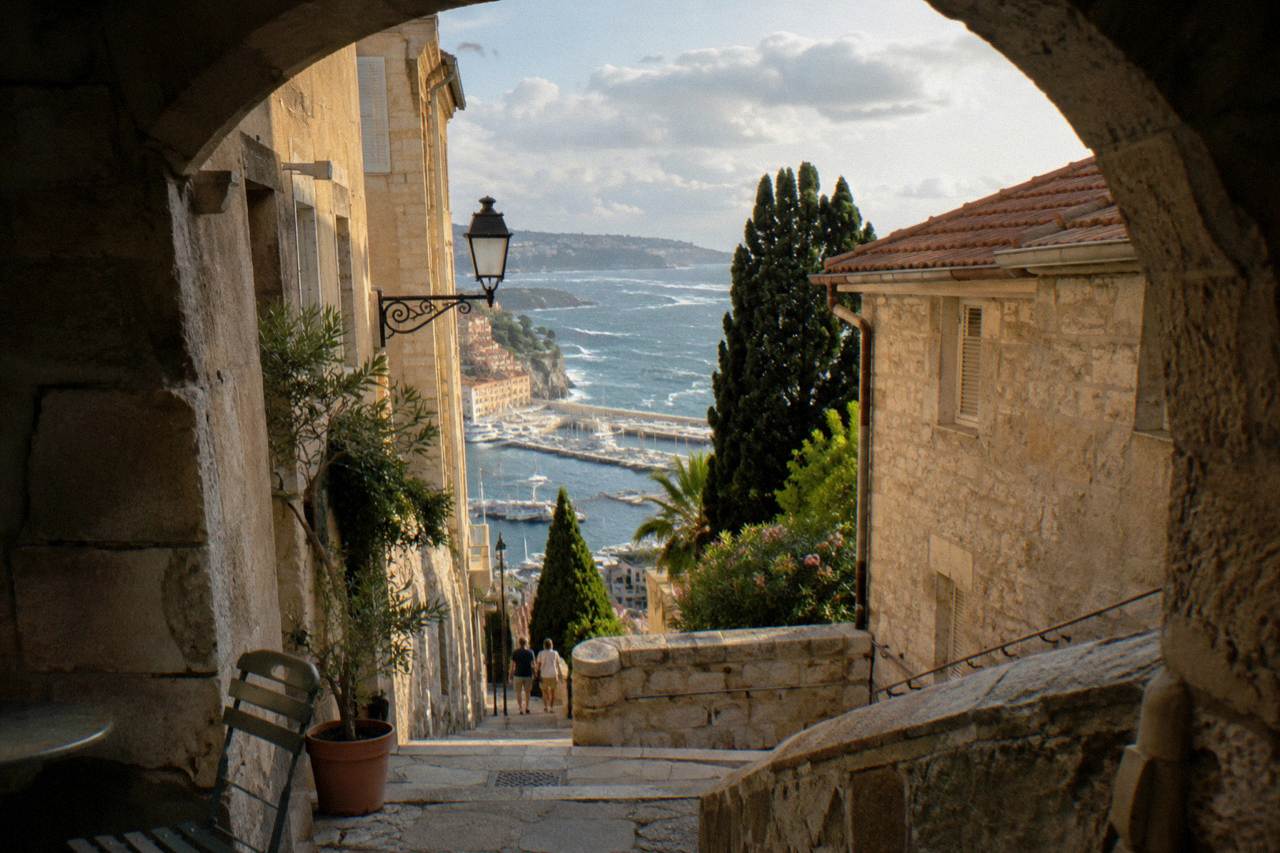 Sunlit Monaco old town street with stone buildings above the Mediterranean harbor